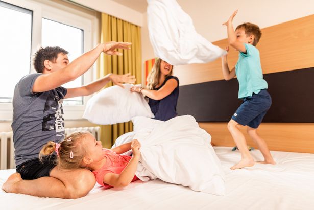 Eine vierköpfige Familie macht eine Kissenschlacht in einem Hotelzimmer. Sie sind in Eibenstock.