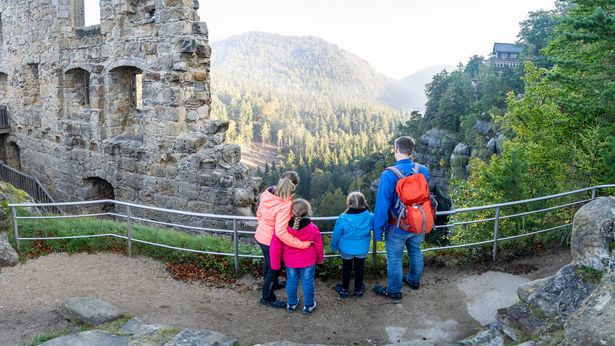 Eine Familie steht auf dem Berg Oybin neben einer Ruine und schaut sich die Landschaft des Zittauer Gebirges an.