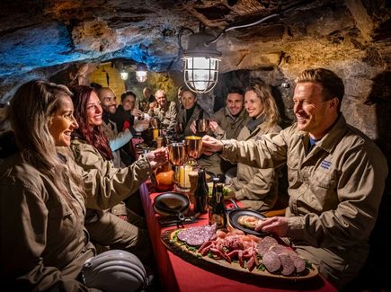 Eine Gruppe macht einen Bergmannsschmaus im Silberbergwerk Reiche Zeche in Freiberg. Sie haben eine Platte auf dem Tisch und stoßen miteinander an.