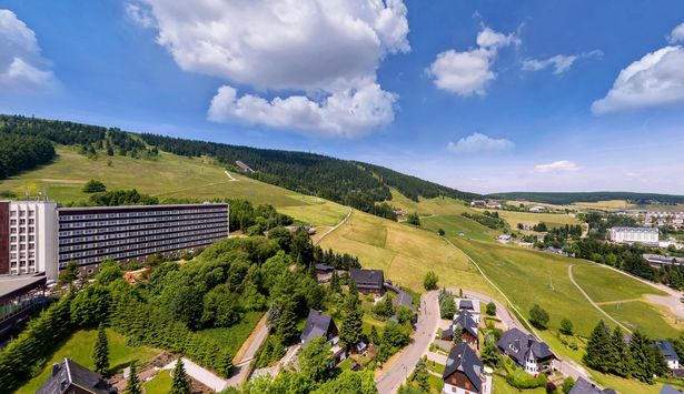 Auf der linken Hälfte ist das Ahorn-Hotel am Fichtelberg zu sehen. Auf der anderen Seite erstrecken sich die Landschaft und die Orte des Erzgebirges.