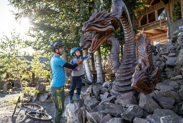 A father stands with his son in front of a dragon sawn out of wood.