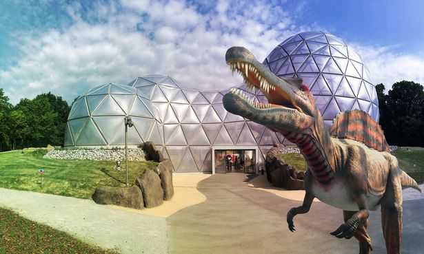 Das Mitoseum, eine Konstruktion aus Stahlrohren, schmückt das Eingangsportal des Saurierpark Kleinwelka. Es ist der Zellteilung nachempfunden. Im Vordergund ist ein Dinosaurier.